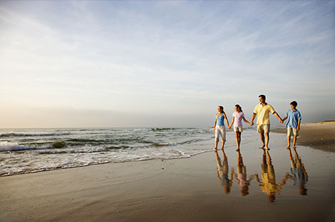 family of four holding hands and walking on the beach