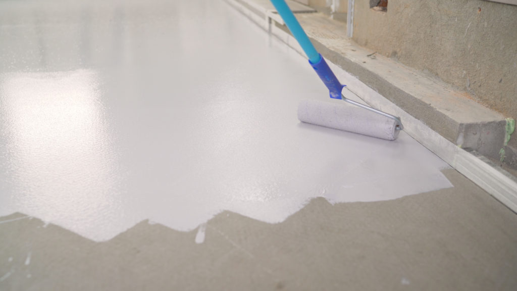 Someone rolling epoxy paint on concrete basement floor